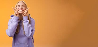 Excited lucky charming friendly blond girlfriend having fun celebrating perfect news best score receive scholarship smiling amused carefree close eyes show peace victory signs, orange background photo