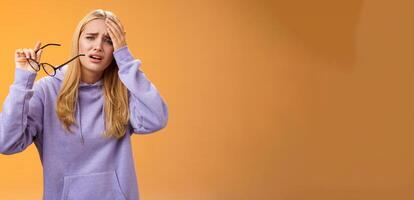 Upset gloomy bothered blond girl take-off glasses cringing grimacing feel unwell suffering headache standing dizzy touching forehead painful migraine bothering working woman, orange background photo