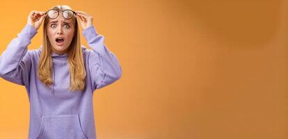 Shocked concerned young woman looking student ruin work staring disturbed upset take-off glasses popping eyes camera gasping speechless terrible acciddent happened, orange background photo