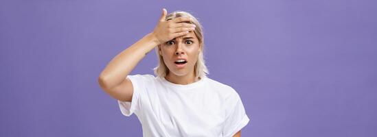 Girl totally forgot about important meeting feeling troubled. Concerned worried good-looking young employee with tanned skin and fair hair holding hand on forehead and frowning from anxiety photo