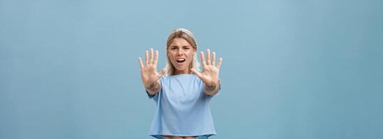 Hold right there. Portrait of intense displeased and irritated attractive young female in blue t-shirt pulling hands towards camera in stop or not gesture frowning and making annoyed expression photo