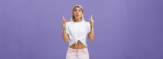 Girl dreaming become flight attendant being amazed with cool airplane flying in sky looking up with surprised impressed look saying wow pointing upwards posing over purple background photo