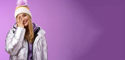 Carefree happy upbeat charming blond woman cover half face tilting head laughing joyfully wearing outdoor stylish silver jacket winter hat having fun awesome five star ski resort, purple background photo