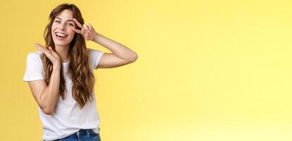 Lively enthusiastic attractive carefree woman enjoy relaxed weekends summer holiday have fun smiling broadly tilt head show peace victory sign joyfully introduce herself posing yellow background photo