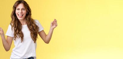 Sassy carefree joyful attractive woman having fun partying listen cool new song favorite artist dancing raise hands up squinting cheeky look camera lip sync hold smartphone yellow background photo