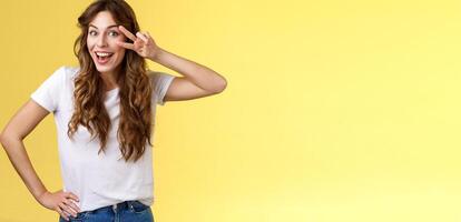 Playful surprised charismatic young caucasian girlfriend having fun look amused enthusiastic show peace victory sign laughing smiling joyfully enjoy summer holidays touch hip stand yellow background photo