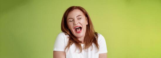 Lazy weekends finally time sleep. Cheerful redhead middle-aged 50s woman yawning satisfied close eyes feel sleepy wake up early morning wanna take nap stand green background watching boring film photo