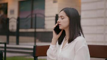 kvinna i vit skjorta är talande på telefon utanför nära modern kontor byggnad. video
