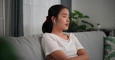 Aufnahmen selektiv Fokus Schuss, entspannt jung Frau tragen kabellos Kopfhörer genießen sich ausruhen Sitzung auf Sofa im Leben Zimmer Hören zu Musik- beim Zuhause video