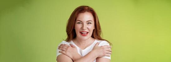 Cheerful charismatic happy good-looking redhead woman red lipstick cross hands chest smiling motivated excited having fun playful thrilled mood grinning enthusiastic standing green background photo