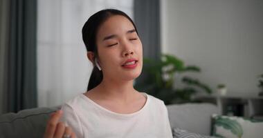 Footage selective focus shot, Relaxed young woman wear wireless headphones enjoying rest sitting on sofa in living room listening to music and dancing at home video