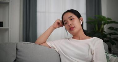 Footage selective focus shot, Relaxed young woman wear wireless headphones enjoying rest sitting on sofa in living room listening to music at home video