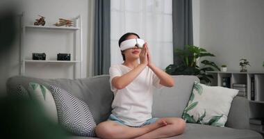 Footage dolly shot, Relaxed young woman wear VR goggles doing yoga and meditation enjoying rest on sofa in living room at home, breathing fresh air, video