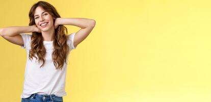 Carefree casual urban girl having summer holiday enjoy sunny perfect warm days wear white t-shirt jeans hold hands neck lazy stretch smiling broadly relaxing resting vacation stand yellow background photo