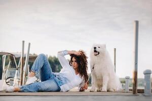 a happy woman with a big white dog lies on a pier near the sea at sunset photo