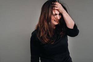 a battered woman in black clothes on an isolated gray background. Violence against women photo