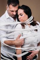 An aggressive man embraces a battered woman and is wrapped in bandages together. Domestic violence photo
