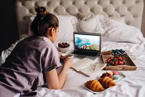 a girl sits in bed in the evening, with a smartphone in her hand and eats strawberries, a girl in bed has sweets before going to bed. photo