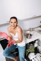 ama de casa niña en rosado guantes después limpieza el casa es emocional y cansado en el blanco cocina, el niña tiene lavado el platos y es descansando y expresando emociones.a lote de lavado platos foto