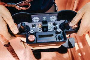 Remote control of a lifting car crane in the hands of a person. A panel with joysticks and buttons for controlling the telescopic bucket of the crane photo