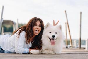 a happy woman with a big white dog lies on a pier by the sea and shows her tongue photo