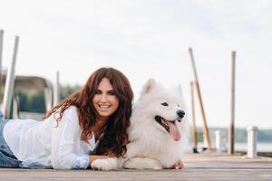 a happy woman with a big white dog lies on a pier near the sea at sunset photo