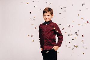 A beautiful boy stands and confetti falls on him on a gray background photo