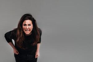 a battered woman in black clothes screams against an isolated gray background. Violence against women photo