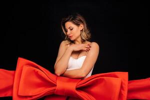 a woman in a white dress in the form of a gift on a black background is wrapped in a festive ribbon photo