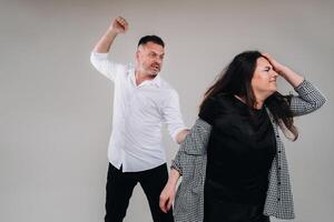 A man swings his hand at a battered woman standing on a gray background. Domestic violence photo