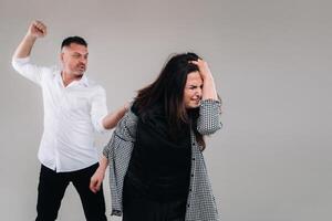 A man swings his fist at a battered woman standing on a gray background. Domestic violence photo