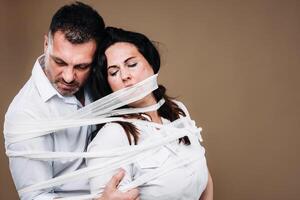 An aggressive man embraces a battered woman and is wrapped in bandages together. Domestic violence photo