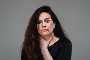 a battered woman in black clothes on an isolated gray background. Violence against women photo