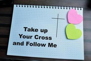 Concept of Take up Your Cross and Follow Me write on book isolated on Wooden Table. photo