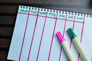 Concept of Weekly Calendar write on book isolated on Wooden Table. photo