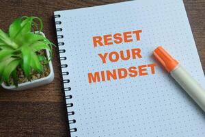 Concept of Reset Your Mindset write on book isolated on Wooden Table. photo