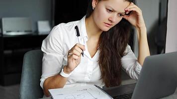 Young tired woman using laptop in home workplace, writing notes, female student learning and watching online webinar or listening audio course, e-learning education concept. High quality 4k footage video