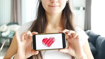 värld hälsa dag begrepp. ung kvinna som visar illustration av hjärta på henne smartphone, illustrerar de betydelse av kardiovaskulär hälsa medvetenhet på internationell hälsa observation. video