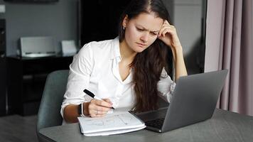 Young tired woman using laptop in home workplace, writing notes, female student learning and watching online webinar or listening audio course, e-learning education concept. High quality 4k footage video