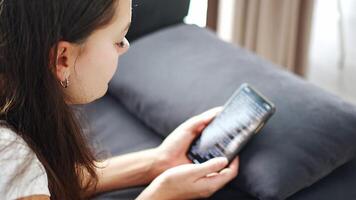 Young smiling woman lying on the sofa and reading a funny online book on her smartphone. High quality 4k footage video