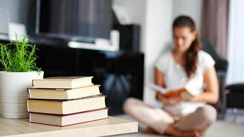 Stack of books in the foreground and woman reading book in the background. High quality 4k footage video