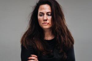 a battered woman in black clothes on an isolated gray background. Violence against women photo