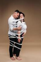 An aggressive man embraces a battered woman and is wrapped in bandages together. Domestic violence photo