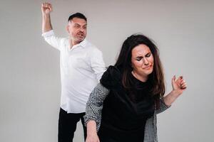 A man swings his fist at a battered woman standing on a gray background. Domestic violence photo