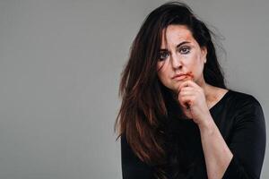 a battered woman in black clothes on an isolated gray background. Violence against women photo