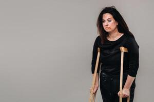 A woman beaten in black clothes with crutches in her hands on a gray background photo