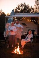 The family is relaxing together by the campfire near their mobile home. Evening family vacation photo