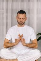 un hombre en blanco ropa de deporte es haciendo yoga con un aptitud habitación. el concepto de un sano estilo de vida foto