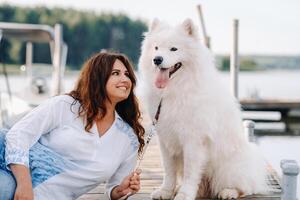 a happy woman with a big white dog lies on a pier near the sea at sunset photo