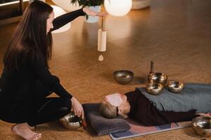 A young beautiful woman is doing a massage with singing bowls and a koshi bell to another girl. Sound therapy photo